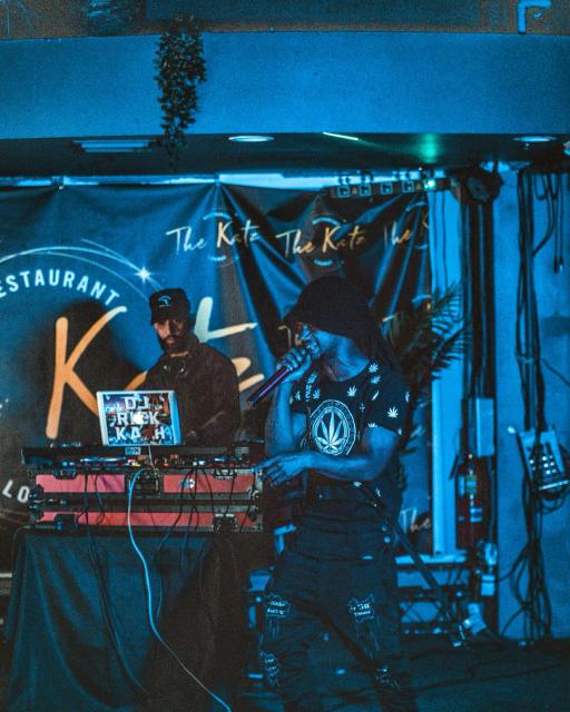 Slim VIP performing live on stage at Katz Lounge, holding a microphone under blue stage lighting with a DJ behind him.