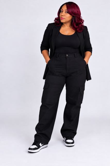 Full-body press photo of Q The Muziq wearing a black blazer and black cargo pants.